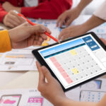 Checkliste Firmenevent planen: Mitarbeiter sitzen am Tisch und besprechen eine digitale Event-Planung auf einem Tablet.