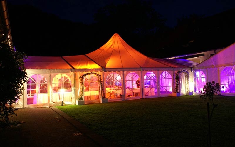 Hochzeit wetterfest planen Ideen: Hochzeitszelt mit transparenten Wänden bei nacht, mit farbenfroher Beleuchtung.
