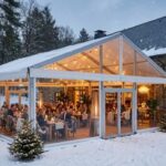 Checkliste Außengastronomie im Winter – Außenansicht eines beleuchteten Restaurants in winterlicher Natur mit einem angebauten, transparenten Winterzeltgarten im Schnee.